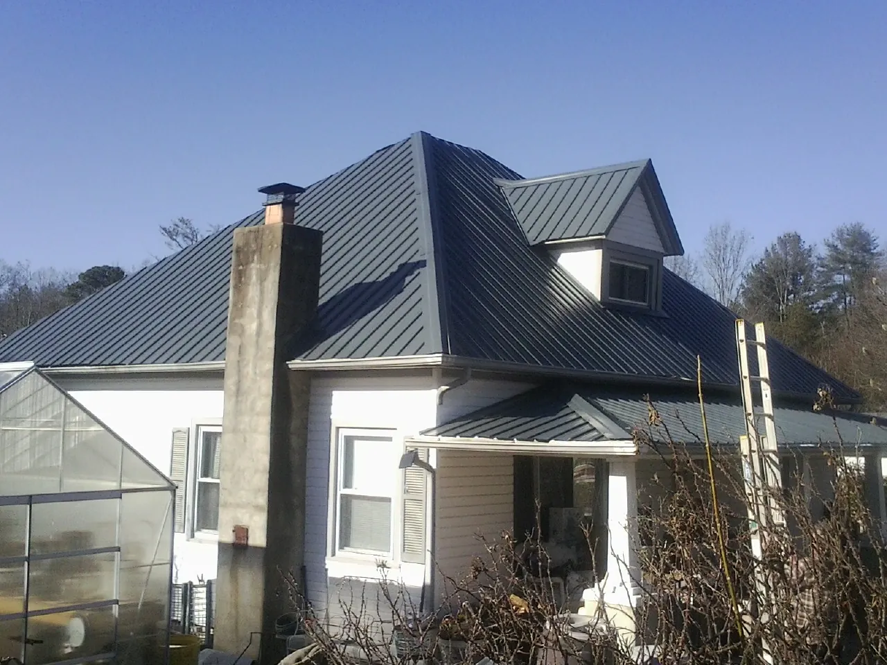 Dark blue standing seam metal roof on a white farmhouse with dormer — Slate & Tile Roof Repair by Roofing Brothers in Essex
