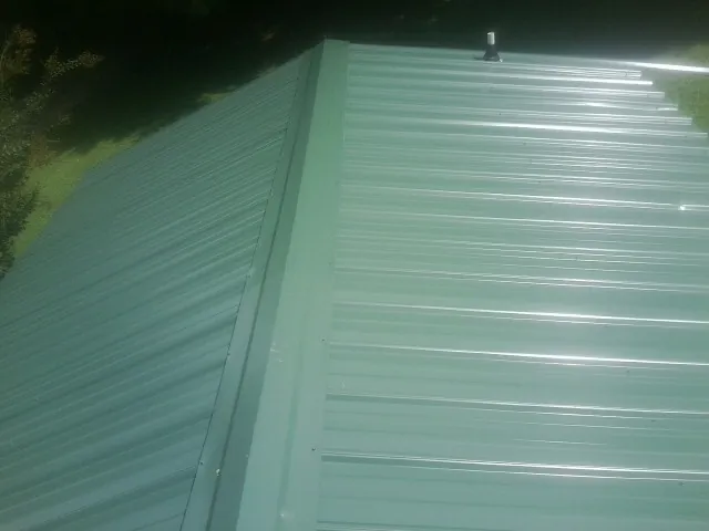 New green metal panels meeting at the ridge of a roof — Flat Roof Repair work by our crew in Essex